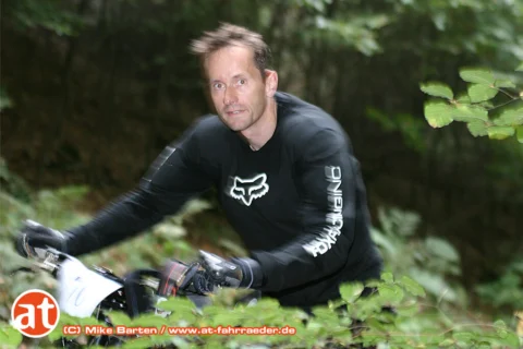 Ein Fahrer im schwarzen Fox-Trikot blickt in die Kamera, das Rad im Vordergrund