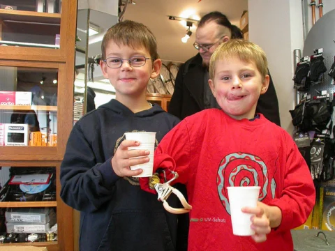 Zwei Jungen halten Becher in die Kamera, dahinter Erwachsene