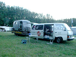 Ein Kleinbus mit at-Logo neben einem VW-Bus auf einer Wiese