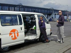 Ein weißer Transporter mit at-Logo, daneben zwei Männer