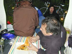 Zwei Personen essen an einem Tisch, dahinter abgestellte Räder
