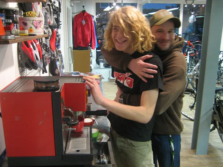 Ole und Blacky lachen an der roten Espressomaschine im Laden
