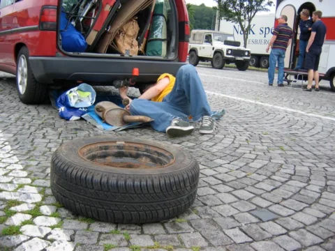 Ein Reserverad und Werkzeug auf Kopfsteinpflaster, dahinter ein offener Kofferraum