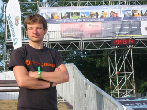 Ein Mann steht mit verschränkten Armen vor einer Zeitmesstafel