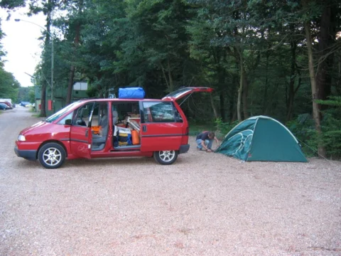 Ein rotes Auto mit offener Heckklappe neben einem Zelt auf einem Campingplatz