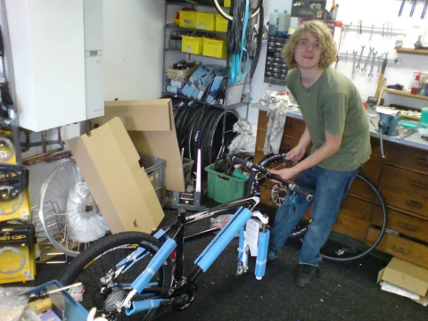 Ein Mann packt ein blaues Fahrrad zwischen Kartons im Laden aus