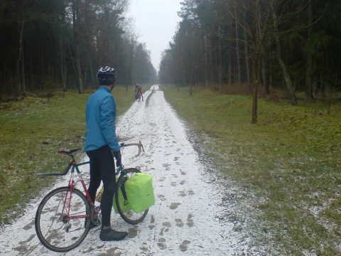 Ein Fahrer steht mit seinem Rad auf einem schneebedeckten Waldweg