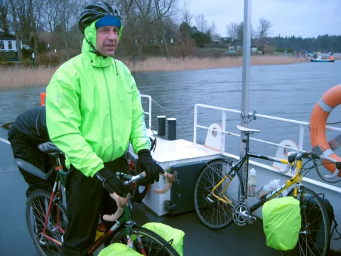 Ein Fahrer in neongrüner Regenjacke mit seinem Rad an Bord einer Fähre