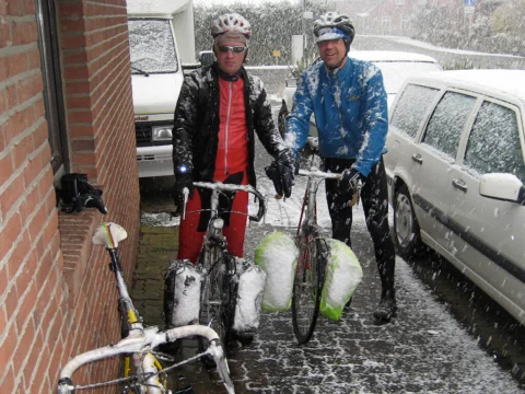Zwei Fahrer mit schneebedeckten Rädern an einer Hauswand im Schneefall