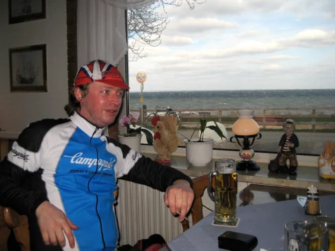 Ein Fahrer im Trikot sitzt mit einem Bier am Fenster eines Lokals