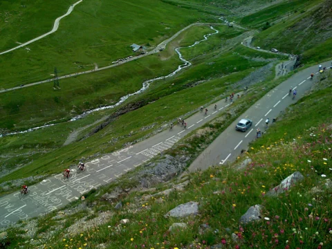 Blick von oben auf die Serpentinen einer Bergstraße durch grüne Wiesen
