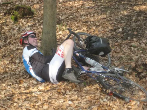 Ein Fahrer liegt erschöpft im Laub neben seinem Rad an einem Baum