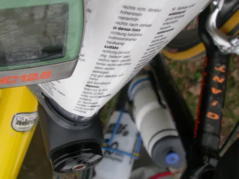 Nahaufnahme eines Radcomputers am Lenker, dahinter eine Bedienungsanleitung