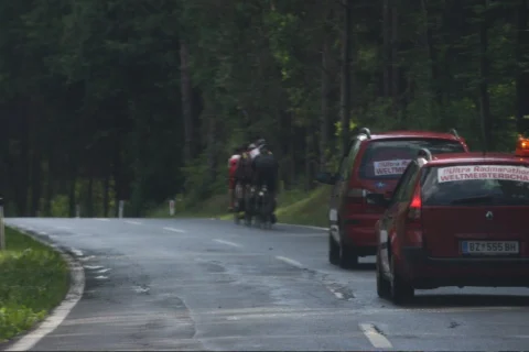Ein Fahrer auf einer Straße im Wald, daneben ein Begleitfahrzeug