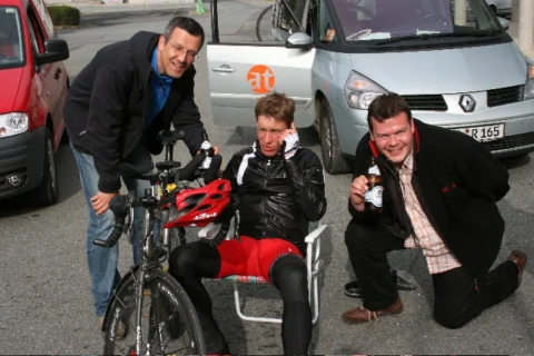 Drei Männer mit Bierflaschen um ein Rennrad, dahinter der at-Transporter