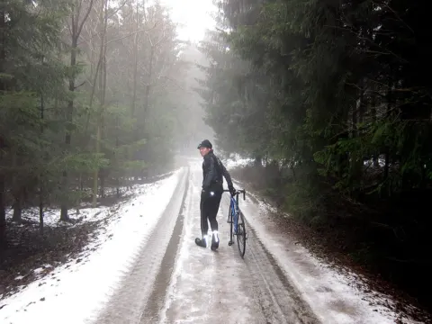 Ein Radfahrer schiebt sein Rad einen matschigen Waldweg im Schnee entlang