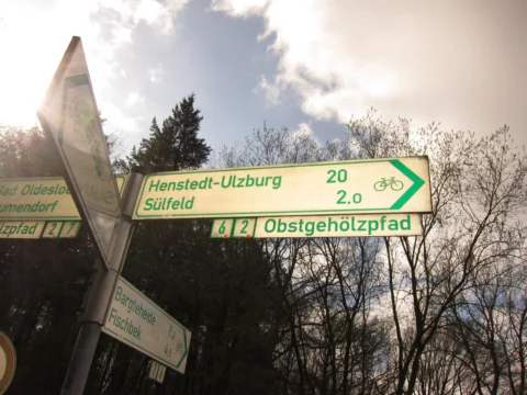 Ein grüner Wegweiser nach Henstedt-Ulzburg und Sülfeld, darunter der Obstgehölzpfad
