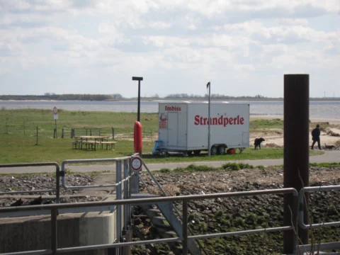 Ein Imbisswagen „Strandperle“ an einem Deich vor dem Wasser