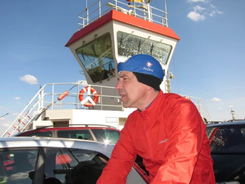Ein Fahrer in roter Jacke an Bord einer Fähre, dahinter das Steuerhaus