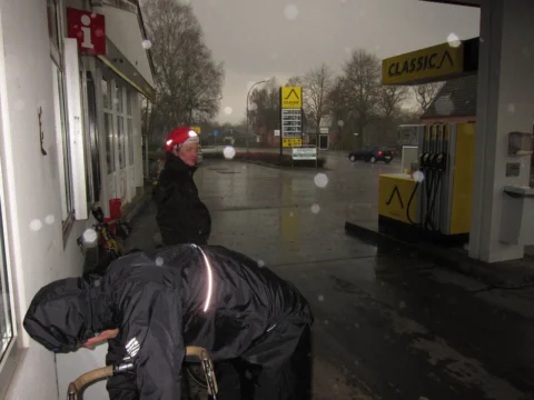 Ein Fahrer zieht sich an einer Tankstelle die Regenjacke an