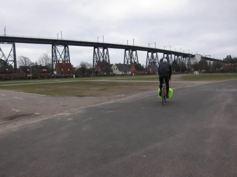 Ein einzelner Fahrer auf einer breiten Straße, dahinter eine Stahlbrücke
