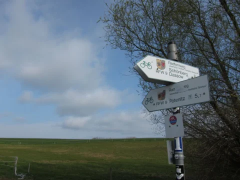 Ein Wegweiser für Radwanderwege vor einem weiten Feld unter blauem Himmel
