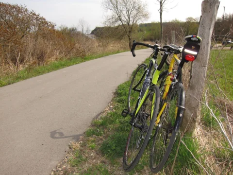 Zwei Rennräder lehnen an einem Zaunpfahl an einer Landstraße