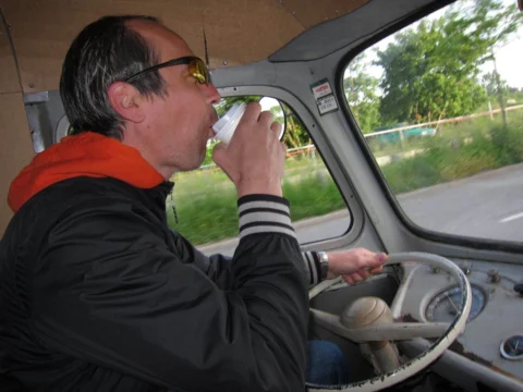 Ein Fahrer trinkt am Steuer eines Oldtimer-Transporters aus einem Becher
