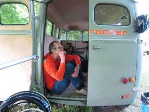 Ein Mann sitzt im offenen Heck des Transporters, davor ein Rennrad