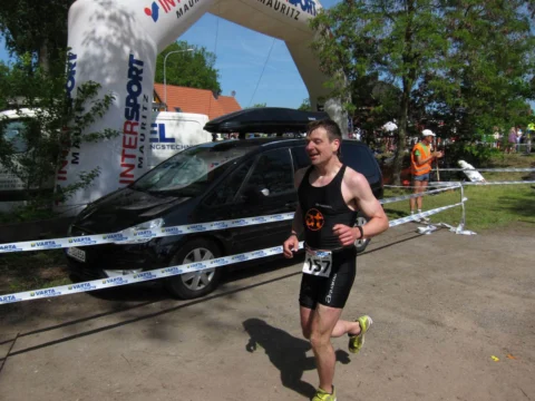 Ein Läufer im Zieleinlauf unter dem Bogen, dahinter geparkte Autos