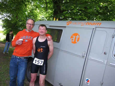 Jens und Petz im Triathlonanzug mit Startnummer 157 vor dem at Mobil, dahinter Fabian