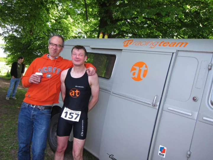 Jens und Petz im Triathlonanzug mit Startnummer 157 vor dem at Mobil, dahinter Fabian