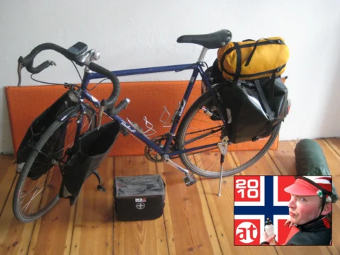 Ein blaues Reiserad mit Packtaschen und gelbem Gepäckrollsack in einer Wohnung