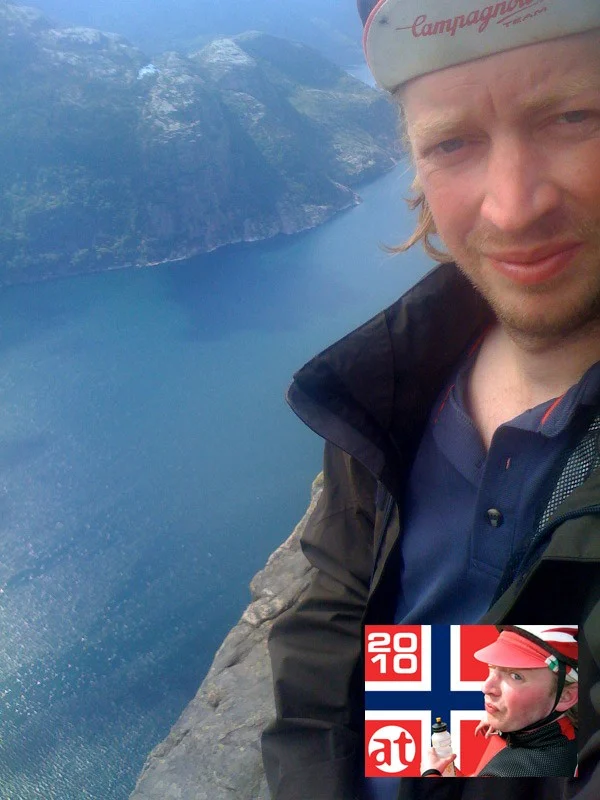 Selfie eines Radfahrers mit Rennmütze über einem Fjord, unten eine Bildmarke mit norwegischer Flagge