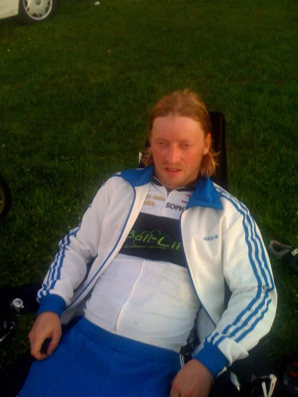 Ein Mann in weiß-blauer Trainingsjacke sitzt auf einer Wiese
