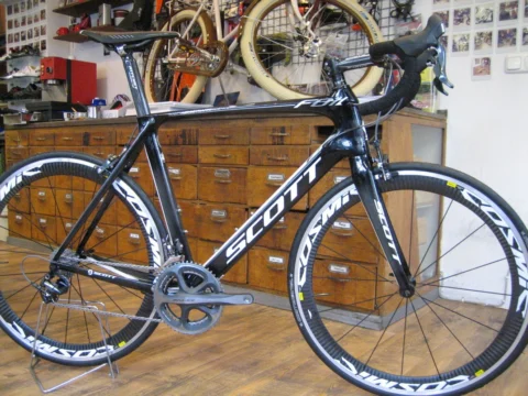 Ein schwarzes Scott-Rennrad mit hohen Laufrädern vor der Schubladenwand im Laden