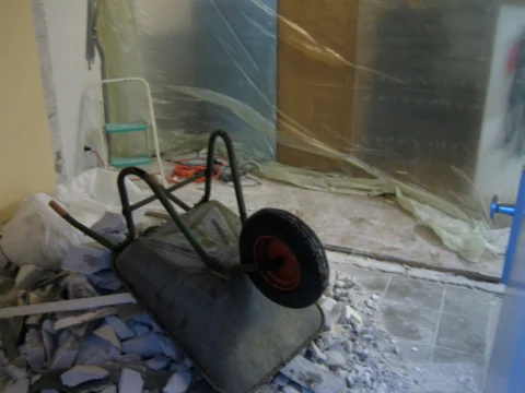 Eine Schubkarre in einem Raum voller Bauschutt hinter einer Staubschutzfolie