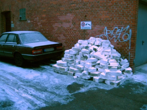 Ein alter Wagen vor einer Backsteinwand, daneben ein Haufen ausgebauter Steine