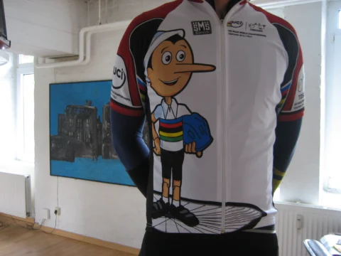 Ein weißes Trikot mit Pinocchio-Motiv und Regenbogenstreifen auf einem Bügel