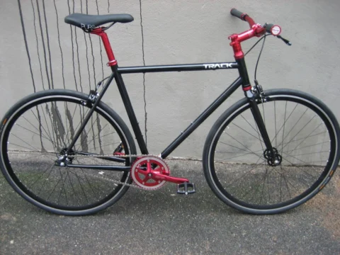 Ein schwarzes Bahnrad mit roter Gabel und rotem Kettenblatt an einer Betonwand