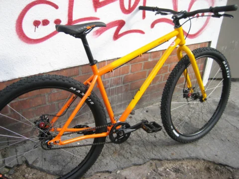 Ein orangefarbenes Rad mit Stollenreifen vor einer Backsteinwand mit Graffiti