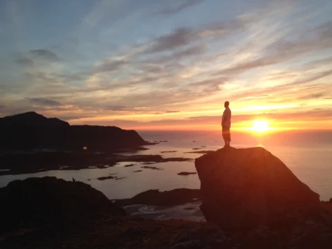 Eine Person steht auf einem Felsen über dem Meer im Sonnenuntergang
