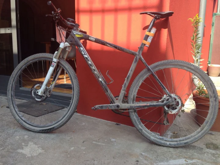 Ein verschlammtes Mountainbike lehnt an einer roten Hauswand