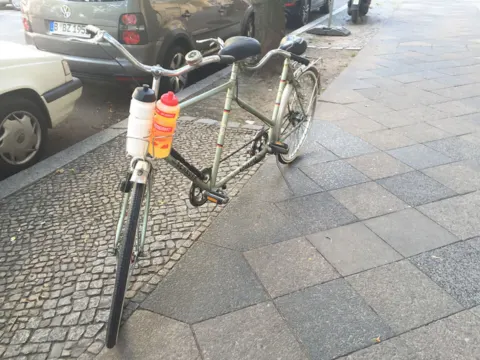 Ein Tandem steht am Straßenrand auf dem Gehweg, dahinter parkende Autos