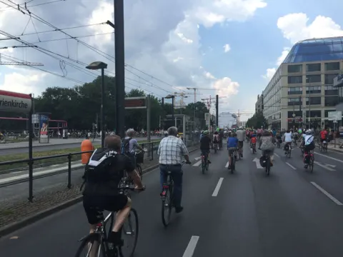 Radfahrende auf einer abgesperrten Stadtstraße unter Wolkenhimmel
