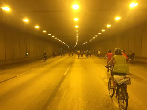 Radfahrende in einem gelb beleuchteten Straßentunnel