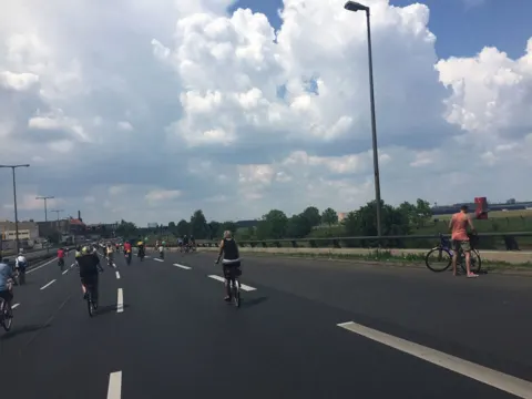 Ein weit gezogenes Feld Radfahrender auf der Autobahn unter Quellwolken