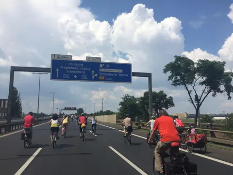Radfahrende unter einer Autobahn-Schilderbrücke