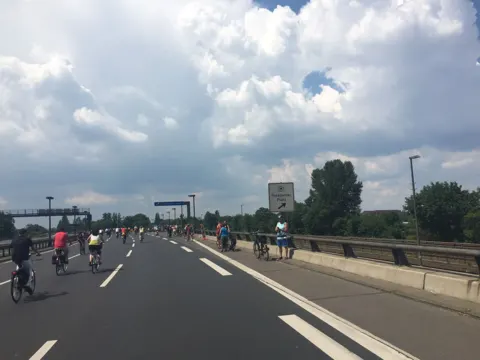 Ein langer Zug Radfahrender auf der Autobahn zwischen Leitplanken