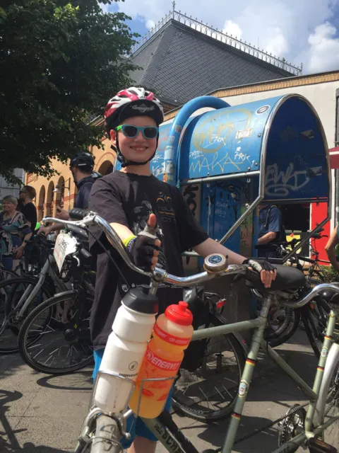 Ein junger Fahrer mit Helm und Sonnenbrille wartet mit dem Rad in einer Gruppe
